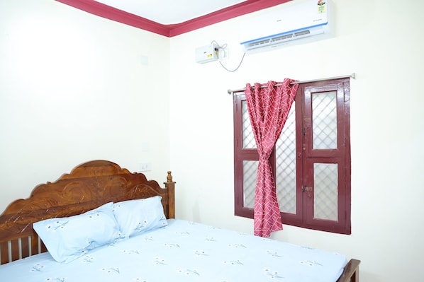 A bedroom with a wooden bed, a window with a red curtain, and an air conditioning unit on the wall.