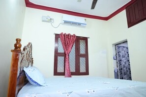 A bedroom with a bed, a window with curtains, an air conditioning unit, and a door.