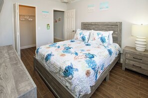 A bedroom with a bed, a nightstand, a wooden bench, a closet, and a door. - Happy Oasis- Relax, Swim & Unwind in Your Tropical Cape Coral Retreat (Cape Coral)