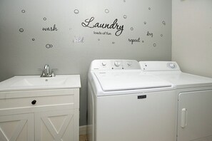 A laundry area with a sink and a front-loading washing machine. - Happy Oasis- Relax, Swim & Unwind in Your Tropical Cape Coral Retreat (Cape Coral)