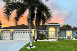 A two-story house with a garage, a driveway, and a well-maintained lawn. - Happy Oasis- Relax, Swim & Unwind in Your Tropical Cape Coral Retreat (Cape Coral)