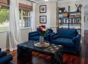 A living room with a blue sofa, a coffee table with a vase of flowers, and a bookshelf with books and decorative items. - Screened HTD Pool/SPA + Game RM + 15 Min to Beach + Luxury Design + Many Beds (Clearwater)