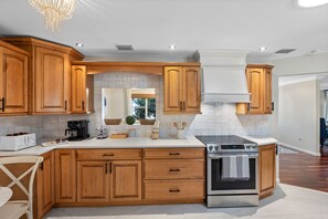 A modern kitchen with wooden cabinets, a built-in oven, and a white countertop. - Screened HTD Pool/SPA + Game RM + 15 Min to Beach + Luxury Design + Many Beds (Clearwater)