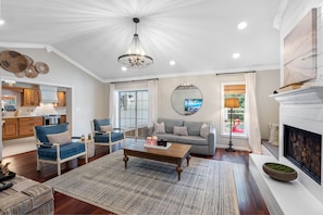 A spacious living room with a fireplace, a dining area with wooden cabinets, and a kitchen visible through an open door. - Screened HTD Pool/SPA + Game RM + 15 Min to Beach + Luxury Design + Many Beds (Clearwater)