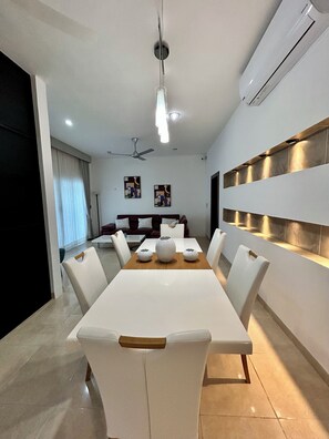 Un'area pranzo moderna con un tavolo bianco, sedie bianche e una ventola a soffitto.