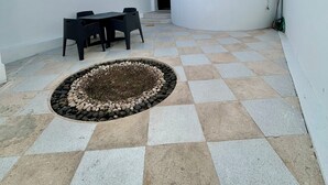 Um pátio com piso xadrez, um canteiro redondo e uma mesa com cadeiras.