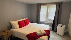 Ett hotellrum med en säng, ett nattduksbord, ett fönster med gardiner och en värmare.