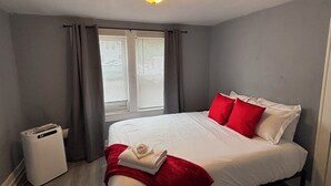 Ett hotellrum med en säng, ett nattduksbord, en värmare och ett fönster med gardiner.