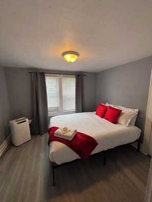 Una habitación de hotel con cama, mesita de noche, calentador y ventana con cortinas.