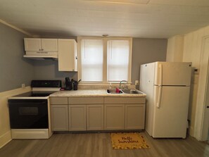 Una cocina compacta con armarios blancos, estufa, lavaplatos y refrigerador.