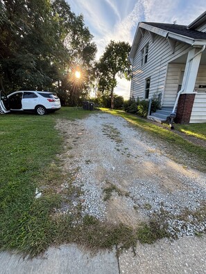 Un camino de entrada residencial que conduce a una casa, con un sendero de grava y un coche aparcado.