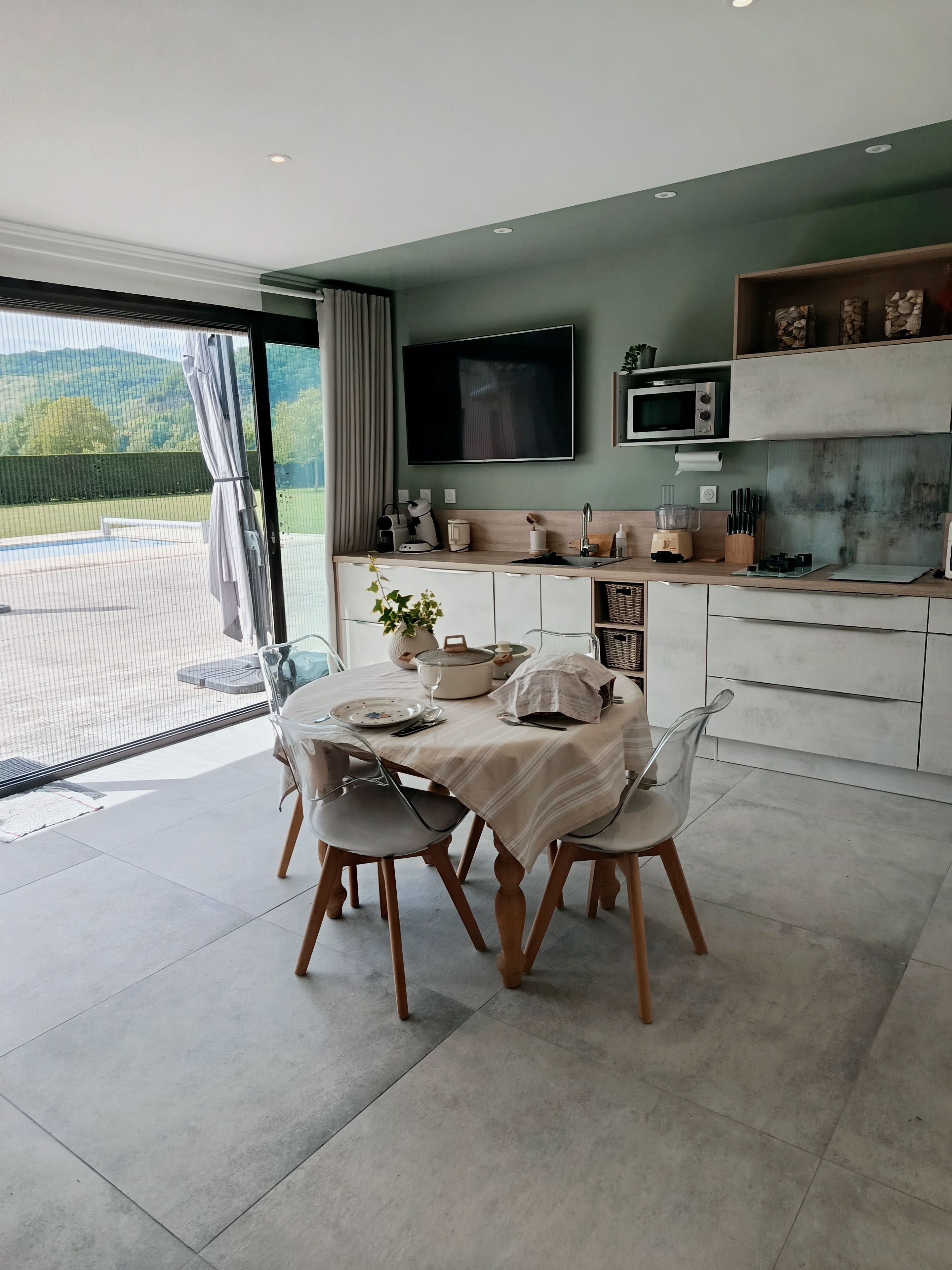 A modern kitchen with a dining area, a flat-screen TV, and a view of the outdoors.