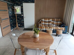 Ein modernes Wohnzimmer mit einem runden Holztisch, klaren Glaskreien, einer Couch mit einem karierten Überwurf und einer Zierpflanze.