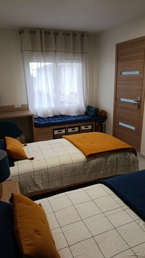 Ein Schlafzimmer mit zwei Betten, einem Schreibtisch, einem Fenster mit Vorhängen und einer Holztür.