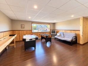 A room with a foosball table, a sofa, a television, and a window with a view of houses. - Comfort & Nature - Alix (Saint-David-de-Falardeau)
