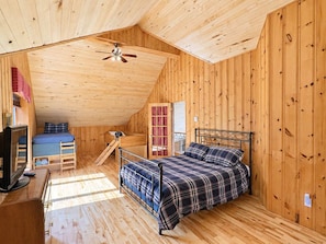A cabin with a loft bedroom, a bunk bed, a desk, and a television.