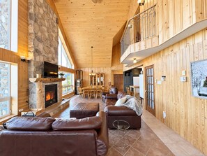 A spacious living area with a stone fireplace, leather sofas, a dining table, and a balcony with a railing.