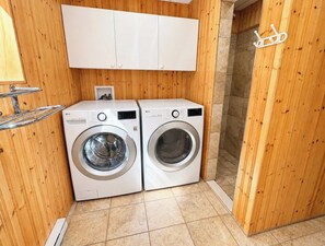 A laundry room with two white washing machines, wooden walls, and a white cabinet above. - Comfort & Nature - Alix (Saint-David-de-Falardeau)
