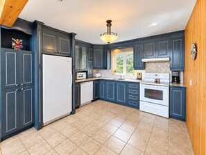 A modern kitchen with dark cabinetry, a white refrigerator, a microwave, a dishwasher, a stove, and a coffee maker. - Comfort & Nature - Alix (Saint-David-de-Falardeau)