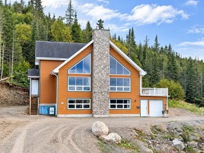 A two-story house with a stone chimney, large windows, and a garage. - Comfort & Nature - Alix (Saint-David-de-Falardeau)