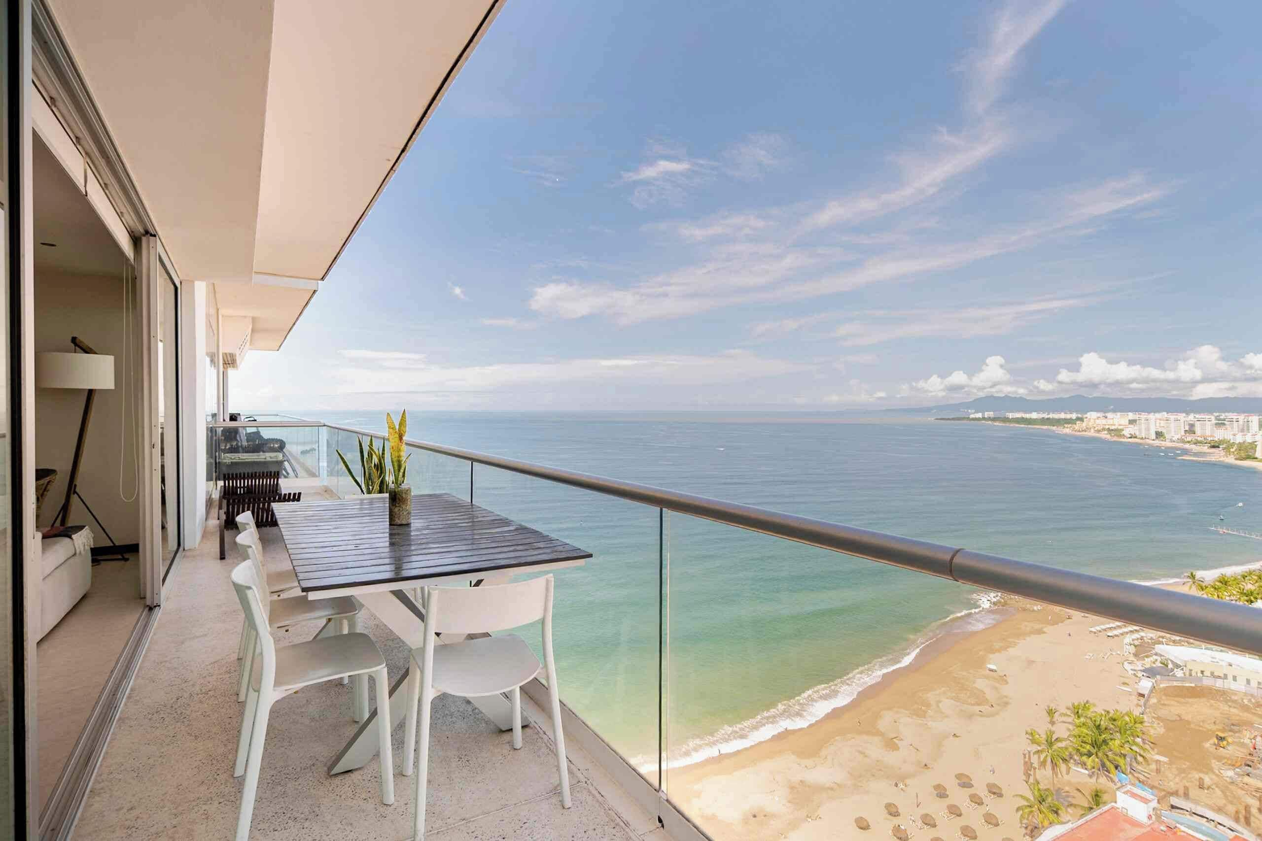 Un balcon avec une table et des chaises, donnant sur une plage et la mer.