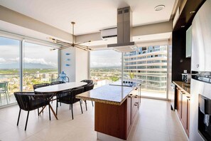 A modern kitchen with a large island, dining area with chairs, and a view of a cityscape through large windows. - Peninsula Puerto Vallarta, near the beach, with ocean and mountain views, 2 bedrooms. (Puerto Vallarta)