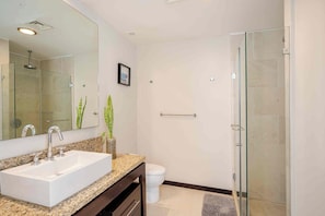 A modern bathroom with a large mirror, a sink, a toilet, and a glass-enclosed shower. - Beachfront Peninsula Puerto Vallarta, ocean and mountain views, 2 bedrooms. (Puerto Vallarta)