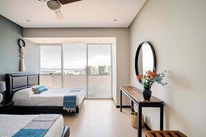 A modern bedroom with a bed, a bedside table with a vase, and a view of the city through large windows. - Peninsula Puerto Vallarta, near the beach, with ocean and mountain views, 2 bedrooms. (Puerto Vallarta)