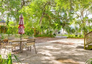 Un espace extérieur aménagé en terrasse, avec une table et des chaises, entouré d’une végétation luxuriante et d’arbres.