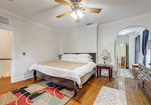 Une chambre à coucher avec un lit, une table de chevet, une lampe, un miroir et un ventilateur de plafond.