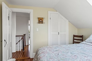 A bedroom with a bed, a wooden chair, a white door, a white closet, and a staircase. - Historic home on Bailey Island with ocean views. Steps from the Giant's Stairs. (Bailey Island)