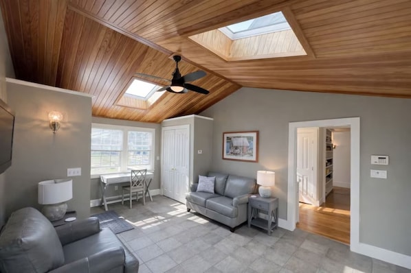 A spacious living room with a sloped ceiling, a ceiling fan, and skylights.