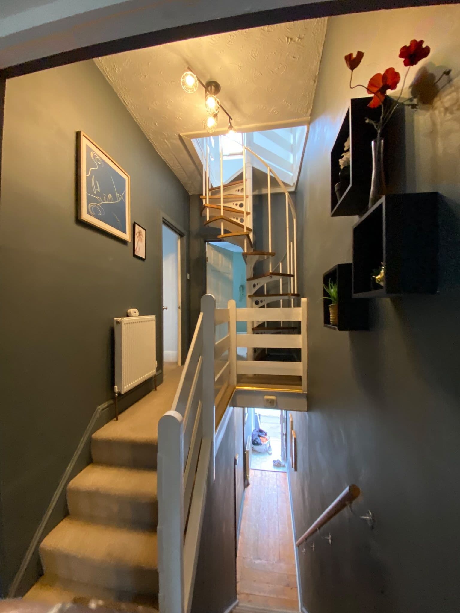 Eine Treppe mit weißer Geländer, die zu einem Zwischenpodest führt, ein Heizkörper an der Wand und ein gerahmtes Bild.