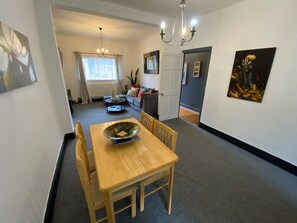 Ein Essbereich mit Holztisch und Stühlen, einer Kristallleuchter und Blick in einen angrenzenden Raum mit einer Couch und einem Fenster.