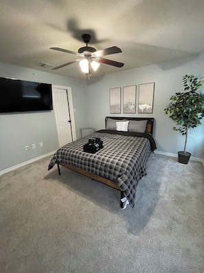 Ein Schlafzimmer mit Bett, Deckenventilator, Wand-Fernseher und einer Zimmerpflanze.