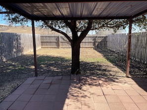 Ein überdachter Patio-Bereich mit einem Baum in der Mitte, umgeben von einem Holenzaun.
