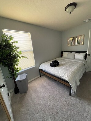 A bedroom with a bed, a window with blinds, a plant, a trash can, and a ceiling light. - Home SWEET Home away from home! Selma, TX! (Selma)