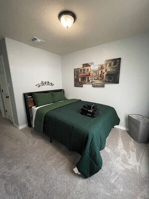 A bedroom with a bed, a wall-mounted picture, a ceiling light, and a trash bin. - Home SWEET Home away from home! Selma, TX! (Selma)
