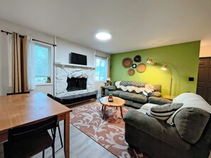 Ein Wohnzimmer mit Kamin, einer Couch, einem Couchtisch und einem Essbereich mit Tisch und Stühlen.