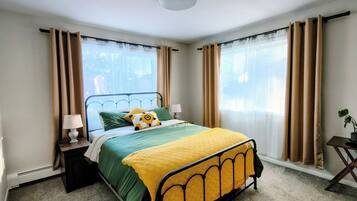 Een slaapkamer met een bed, een nachtkastje, een lamp, een stoel en een raam met gordijnen.