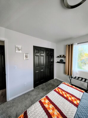 Een slaapkamer met een bed, een kledingkast, een raam met gordijnen en een wandplank.
