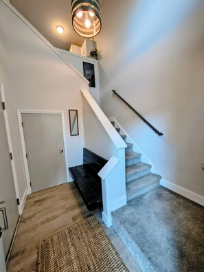 Un escalier muni d’une rampe, dont les marches sont recouvertes de moquette, et un luminaire placé au-dessus.