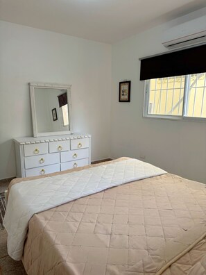 Une chambre à coucher comprenant un lit, une commode, un miroir, une fenêtre et un appareil de climatisation.