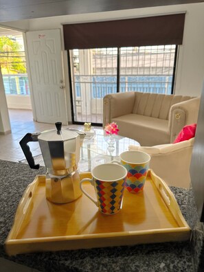 Un plateau avec une machine à café et deux tasses sur une table, un canapé et une porte en arrière-plan.