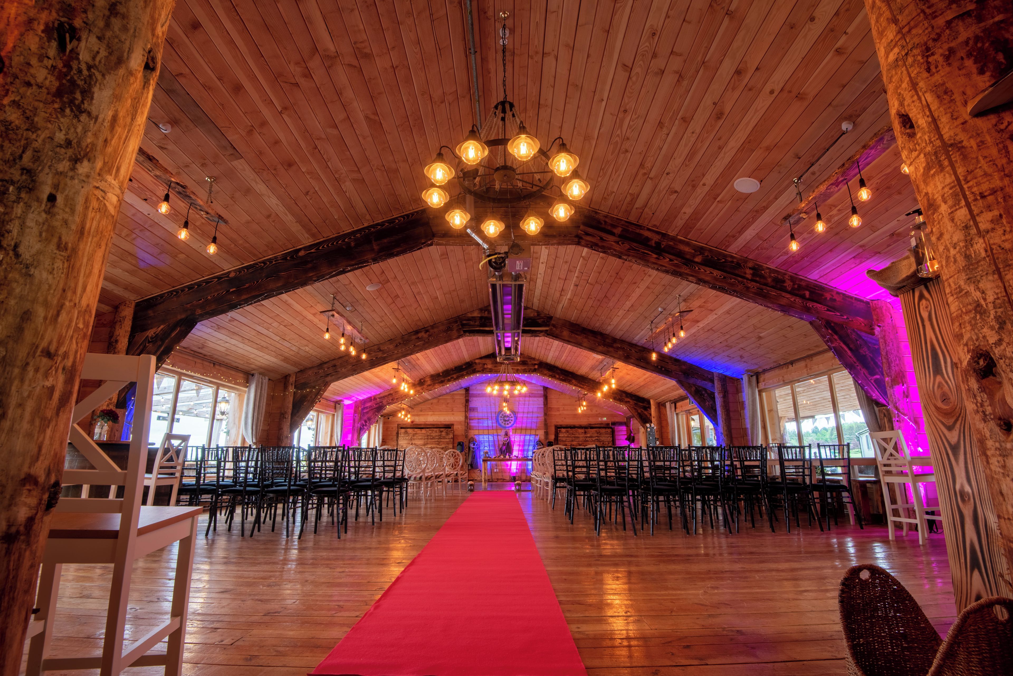 A spacious hall with a wooden ceiling, rows of chairs, and a red carpet leading to a stage.