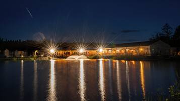 A lakeside property with a wooden building, a dock, and a fountain.