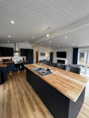 A modern kitchen with a central island, black cabinetry, and a wooden countertop.