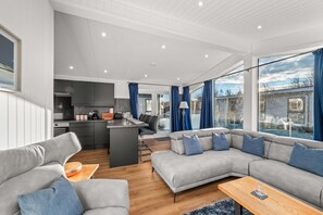 A modern living room with a grey sectional sofa, a wooden coffee table, and a kitchen area with dark cabinets and a black kettle. - Silverwood Resort & events Barn  (Perth)