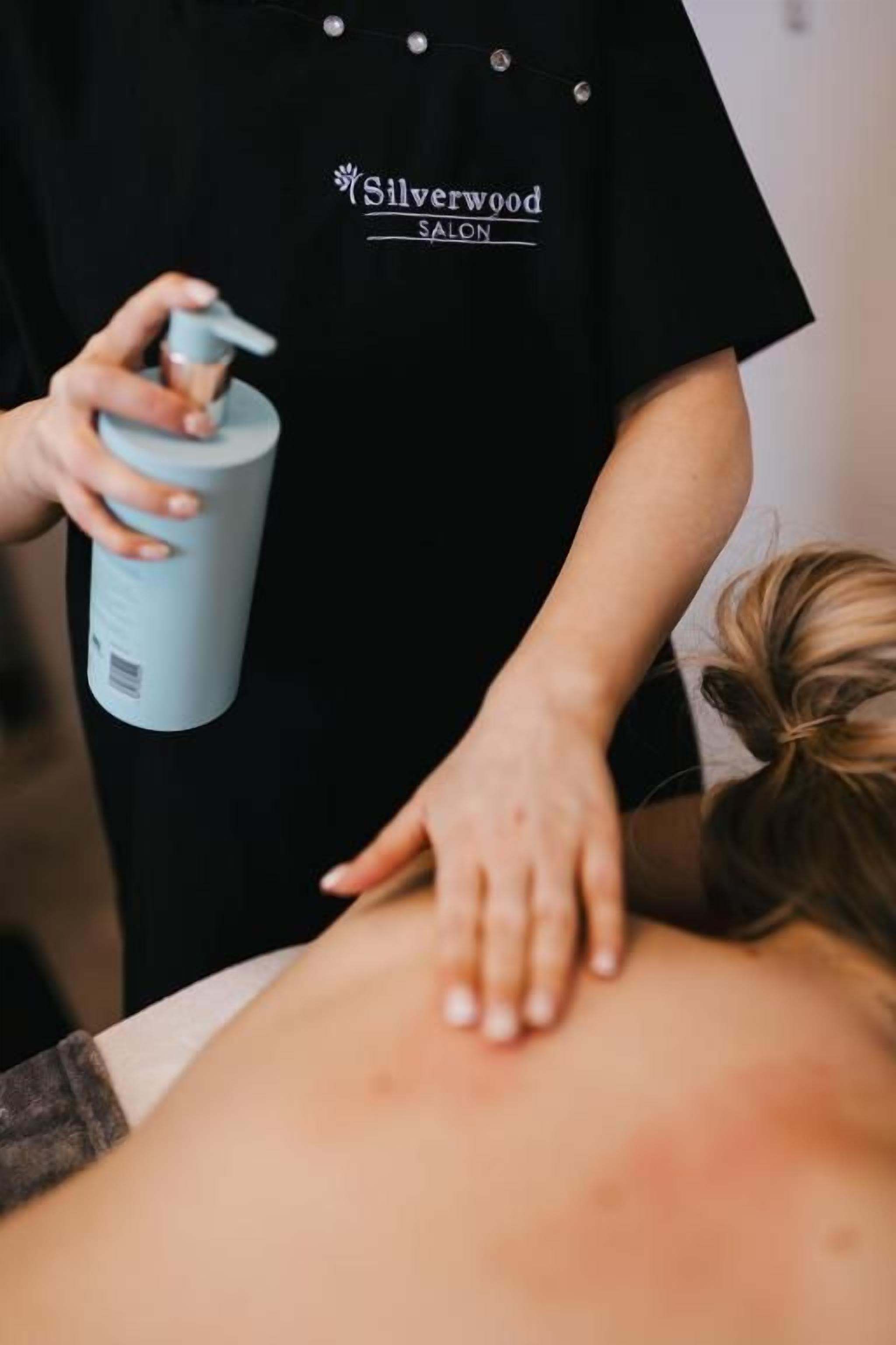 A person receiving a back massage with a massage oil bottle.