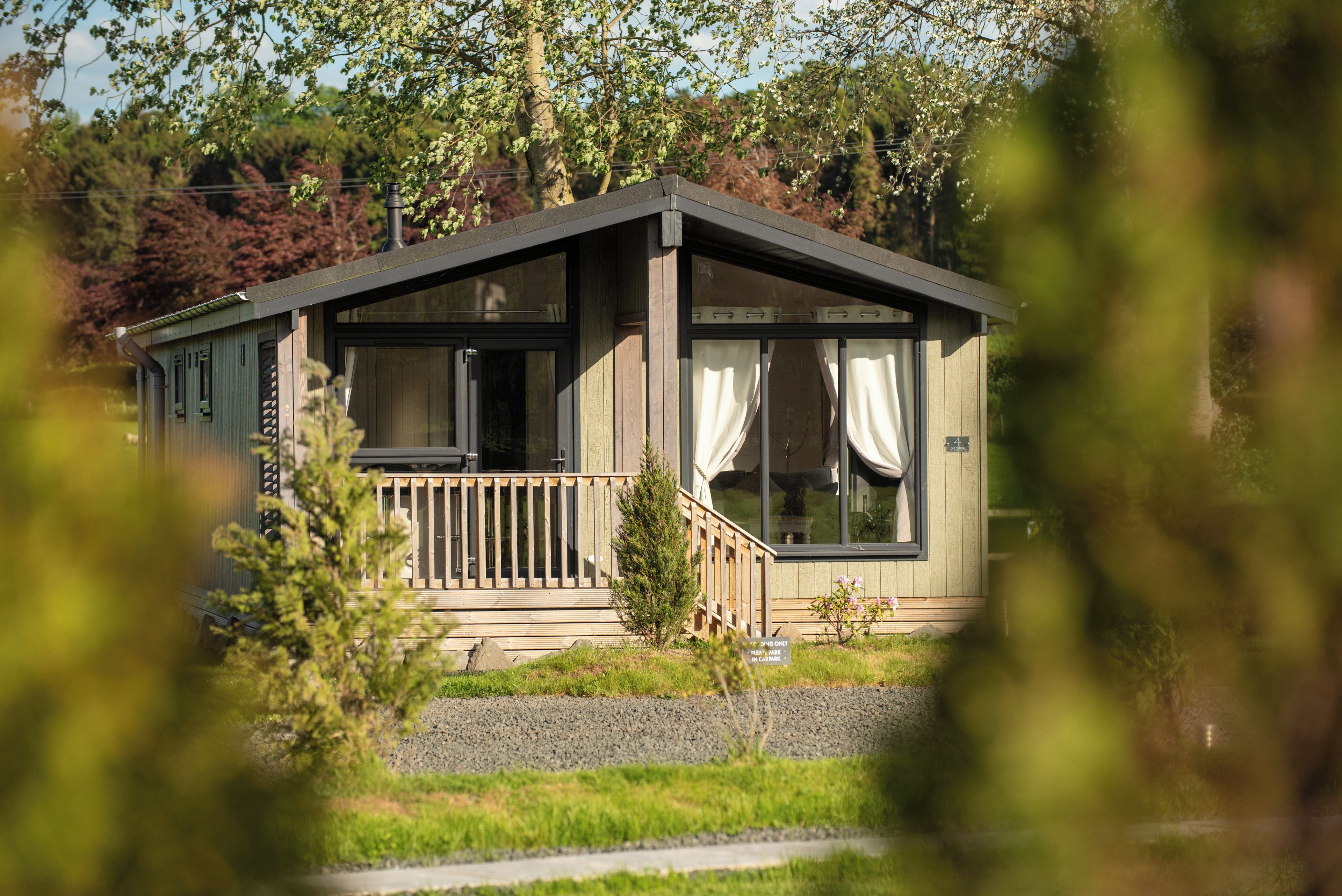 Une cabane dotée d’une terrasse en bois, de grandes fenêtres et d’un petit porche.